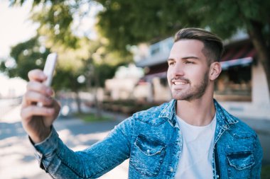 Sokakta mofil telefonuyla selfie çeken çekici bir gencin portresi. Teknoloji konsepti.