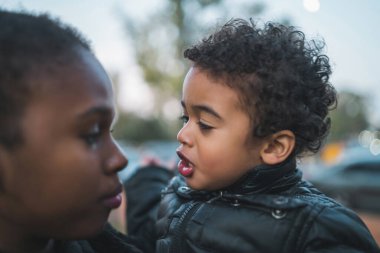 Afrika kökenli Amerikalı bir annenin portresi. Oğluyla parkta durmuş, eğleniyor. Monopental Ailesi.