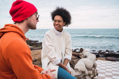 İki genç arkadaşın portresi, arka planda deniz otururken birlikte iyi vakit geçirip sohbet ediyorlar..