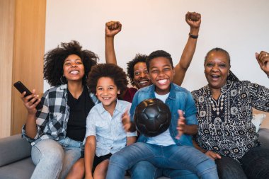 Mutlu Afro-Amerikan çoklu nesil ailesi evdeki oturma odasında televizyonda futbol maçı izliyor. Aile ve spor konsepti.