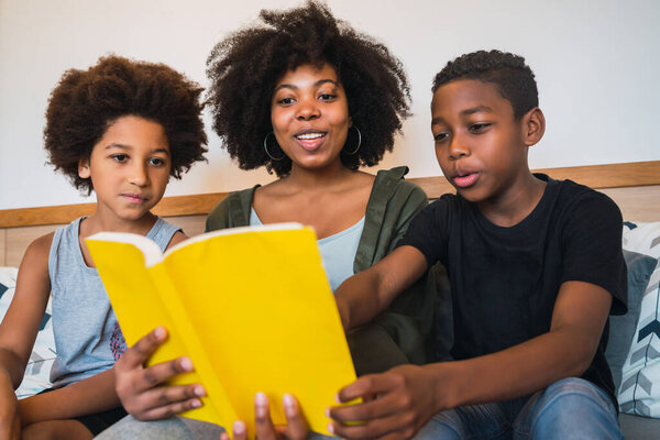 Portrait of Afro American mother reading a book to her children at home. Family and lifestyle concept.