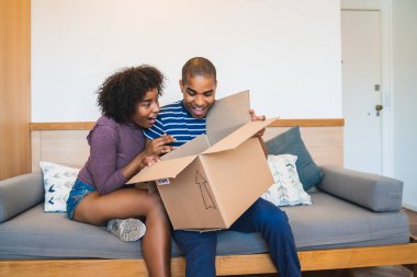 Mutlu genç Latin çiftin portresi evde bir paket açıyor. Teslimat, nakliye ve posta hizmeti konsepti. İnternetten al ve evde kal. Covid-19 Karantina.