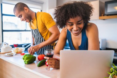 Laptop kullanan ve evde yemek pişirirken yemek tarifi öğrenen genç bir Latin çifti karantinaya aldık. Evde kal. Covid-19. Pandemik önleme.