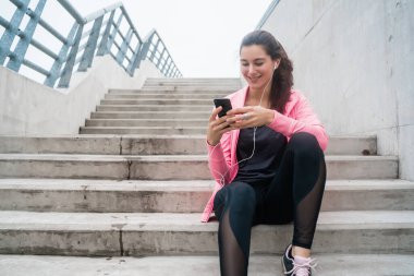 Eğitime ara verdiğinde cep telefonunu kullanan atletik bir kadının portresi. Spor ve sağlık yaşam tarzı.