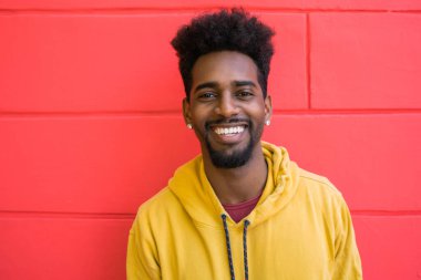 Genç Afro-Amerikan bir adamın portresi. Kendinden emin görünüyor ve kırmızı duvara karşı poz veriyor..