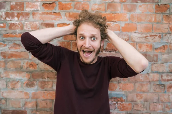 Caddedeki tuğla duvara karşı şok edici hareketlerle genç beyaz adamın portresi. Şehir konsepti.