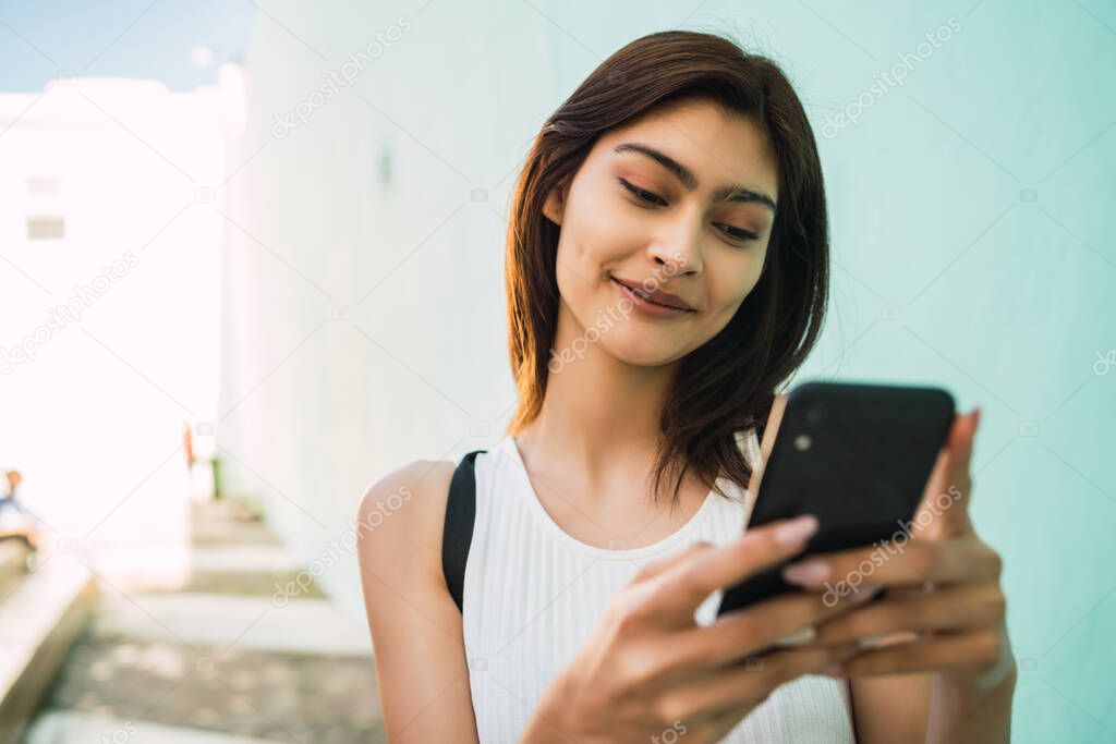 Portrait of young latin woman using her mobile phone outdoors in the street. Urban and communication concept.