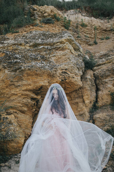 Romantic young fiancee in wreath under veil, alfresco on beach