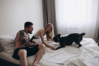 Yatağın üstüne oturan ve evde köpekle oynamayı çift