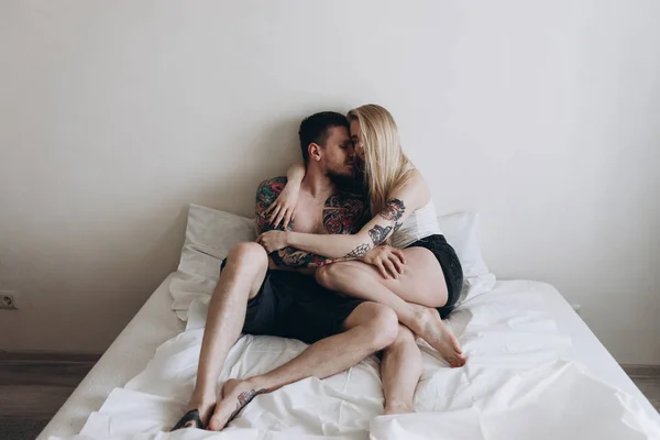 Young tattooed couple sensually embracing on bed at home