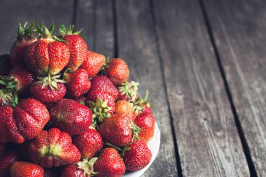 Olgun kırmızı çilekler, beyaz tabakta, siyah tahtada.