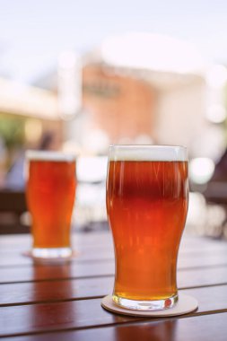 Arka planda sahnesi olan ahşap bir masada iki bardak el yapımı bira. Solgun bira. Sığ alan derinliği