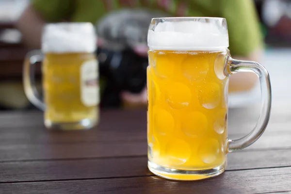 Glass of tapped craft beer. Pale ale on a pub table. Man drinking in background. Shallow depth of field