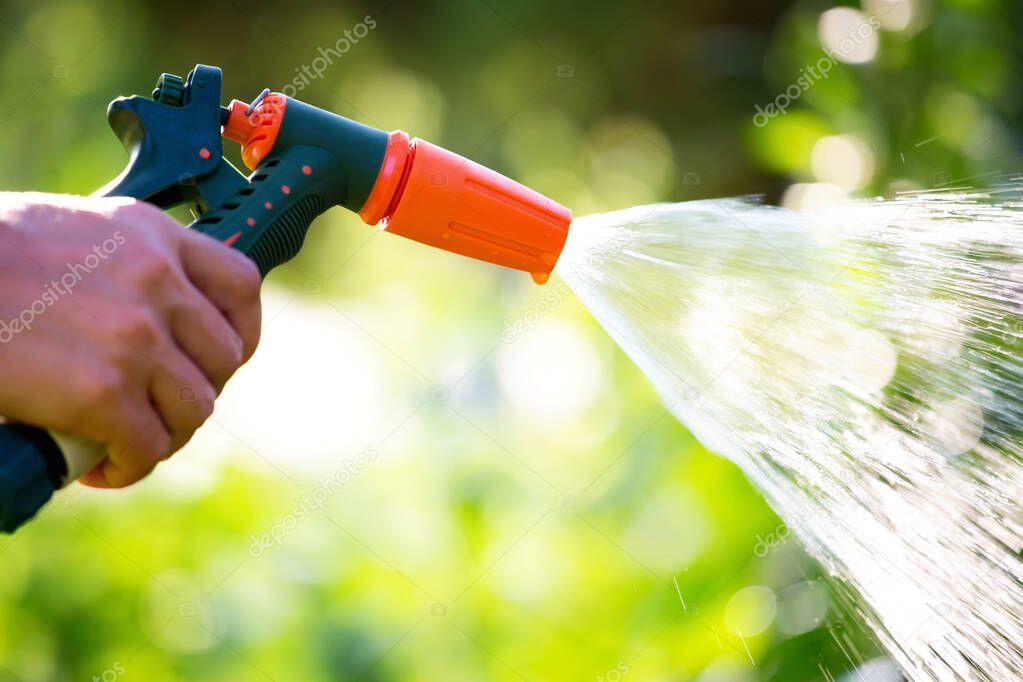 Hose garden sprinkler in woman hand. Watering garden with gun nozzle. Shallow depth of field