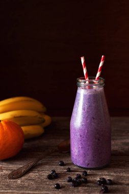 Muz ve yaban mersininden yapılmış organik meyve suyu pipetle birlikte cam bir şişede. Yüzeyin derinliği. Şişenin üst yarısına odaklan.