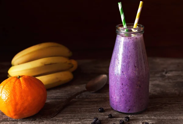Muz ve yabanmersininden yapılmış cam bir şişedeki taze mor smoothie. Sığ alan derinliği