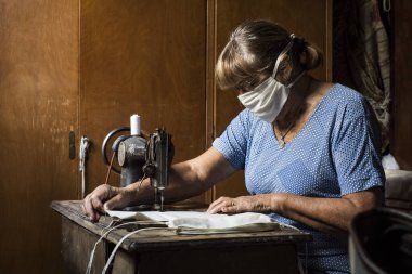 Büyükanne karantinada eski dikiş makinesiyle maske ya da çene bağı yapıyor.