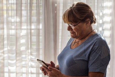 Yaşlı kadın akıllı telefonuyla yeni teknolojiler kullanıyor.