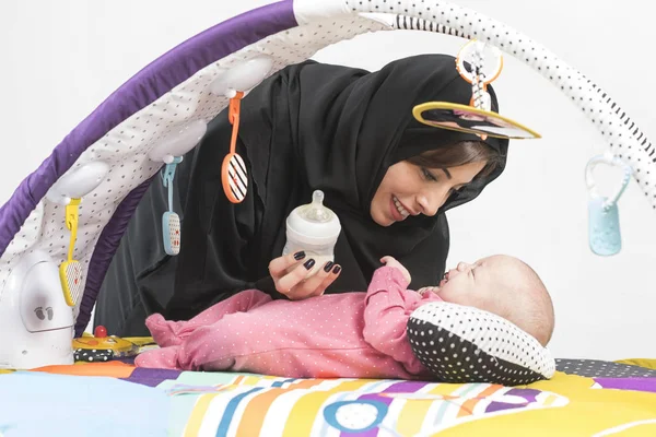 Arabische moeder haar babymeisje voeden op een play-mat — Stockfoto