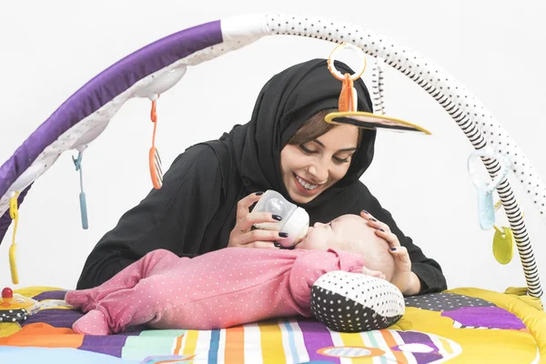 Arabische Mutter füttert ihr kleines Mädchen auf einer Spielmatte — Stockfoto