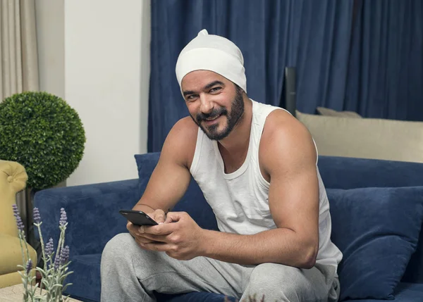 Chico guapo usando teléfono inteligente, hombre guapo sentado en el sofá en — Foto de Stock