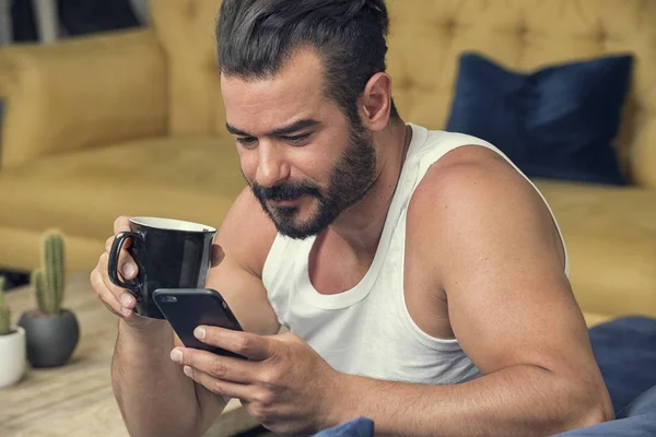 Bel ragazzo che beve caffè e usa il suo smartphone nel mor — Foto Stock