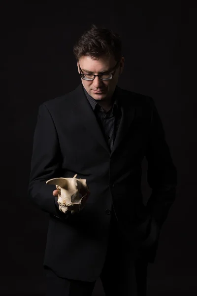 Mand iført en sort dragt holder et dyr kranium og tænker på livet på jorden - Stock-foto