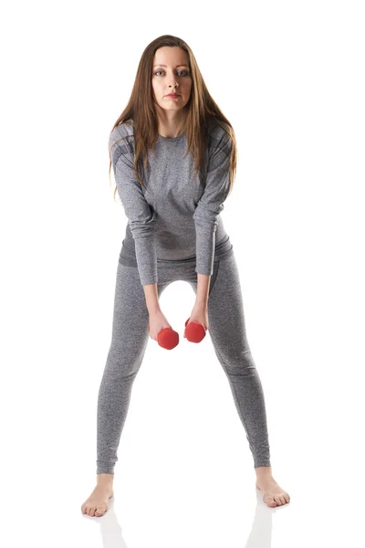 Attraktive braunhaarige Frau in Sport-Thermounterwäsche, die Übungen mit roten Hanteln macht — Stockfoto