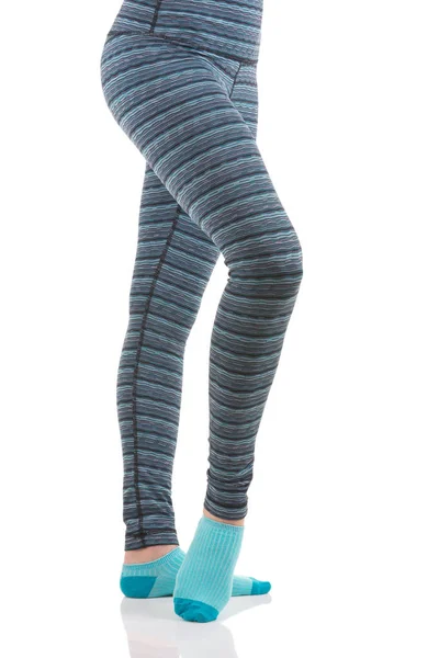 Close up view of woman legs in colourful striped thermal pants and blue socks from the side view standing on one leg with other leg raised — Stock Photo, Image