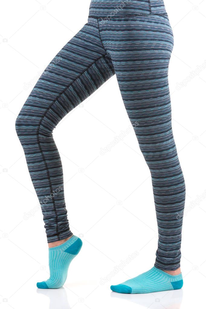Close up view of woman legs in colourful striped thermal pants and blue socks from the side view standing on one leg with other bent at the knee leg