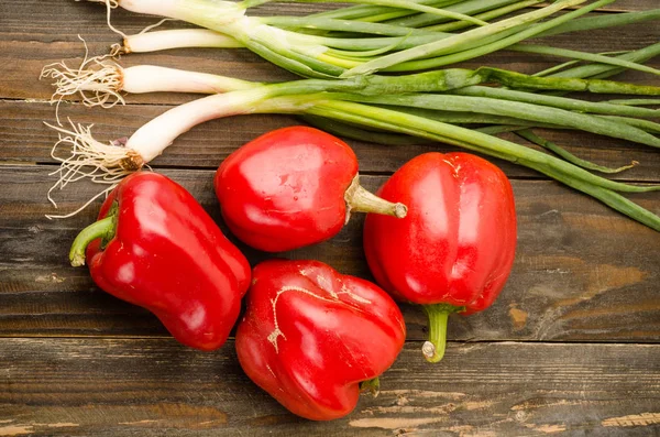 Rote Paprika und Frühlingszwiebeln auf Holzgrund — Stockfoto