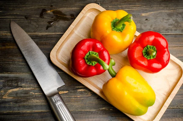 Червоний і жовтий болгарський перець на дерев'яній тарілці та ножі для приготування їжі — стокове фото