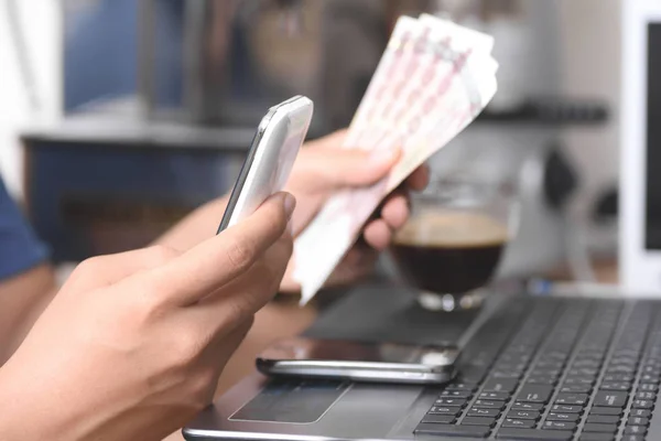 Mano sosteniendo el dinero para pagar a través de teléfono inteligente o portátil — Foto de Stock