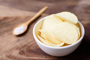 Bir kase ve kaşık tuz ahşap arka plan üzerinde patates cipsi