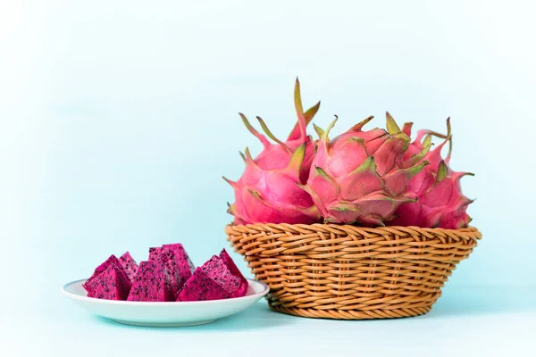 Sliced red dragon fruit on white plate and basket on pastel background, tropical fruit