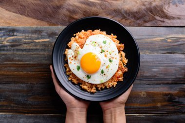 Elle tutulan siyah tabakta kızarmış yumurtalı kimchi pilavı, Kore yemeği, üst manzara.
