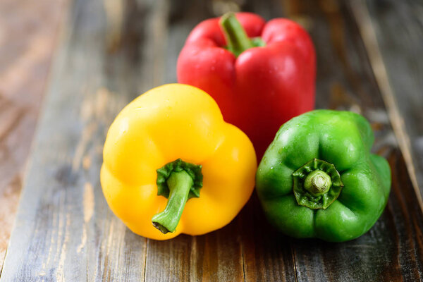 Yellow, green and red bell peppers on wooden background, organic vegetables