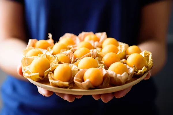 Cape gooseberry fruit (golden berry or physalis) on wooden plate holding by hand