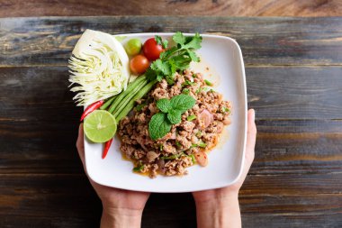 Tayland yemeği, baharatlı domuz salatası (Larb Moo) beyaz tabak üzerinde ahşap arka planda, Tayland 'ın kuzeydoğusunda popüler yerel yemekler, Top view