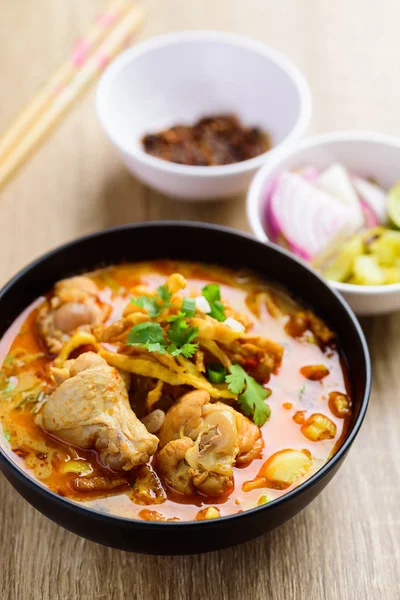 Traditional Northern Thai food (Khao Soi), spicy curry noodles soup with coconut milk and chicken eating with crispy deep-fried egg noodles, pickled mustard greens, shallots, lime, coriander leaves and ground chillies fried in oil