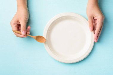 Biyolojik çözünebilir plaka, gübrelenebilir plaka ya da pastel arka planda kaşık tutan tek kullanımlık eko plaka, üst görünüm