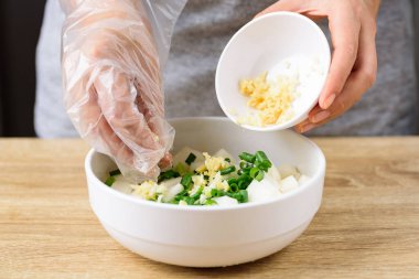 Kimchi turp pişirme, üçüncü adım; dilimlenmiş taze soğan, zencefil, sarımsak ve turpu bir kasede karıştırmak.