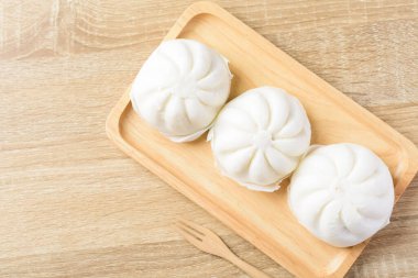 Domuz kıymalı buğulanmış çörekler ve ahşap tabak ve çatalla tuzlanmış Asya yemekleri.