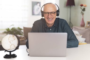Man listening to music on headphones while working on the computer from home - Middle aged man having fun in conference - warm contrast filter