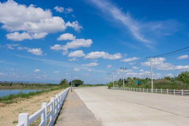 Concrete road with white fence and street lamp in day blue sky background. clipart