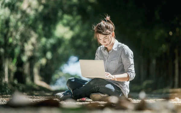asian women sitting relax on the ground and play white laptop computer in forest tree