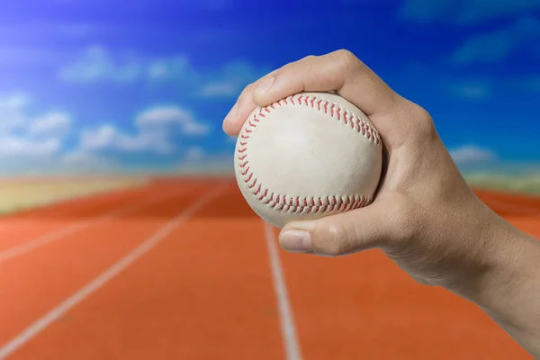 Mano che tiene una palla da baseball su pista da corsa rossa con cielo blu — Foto Stock