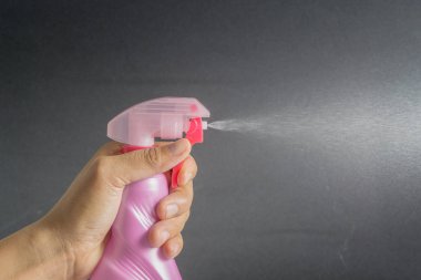 el tutma pembe sprey plastik şişe ve koyu arka plan üzerine püskürtme kapatın.