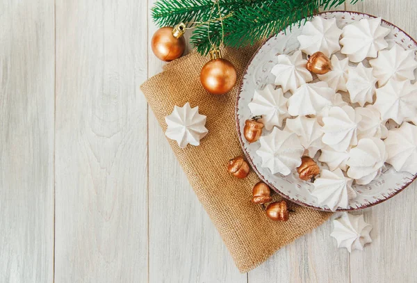 Dolce sfondo natalizio con meringhe ariose, ramo di abete, ghiande dorate e palle sul piatto. — Foto Stock