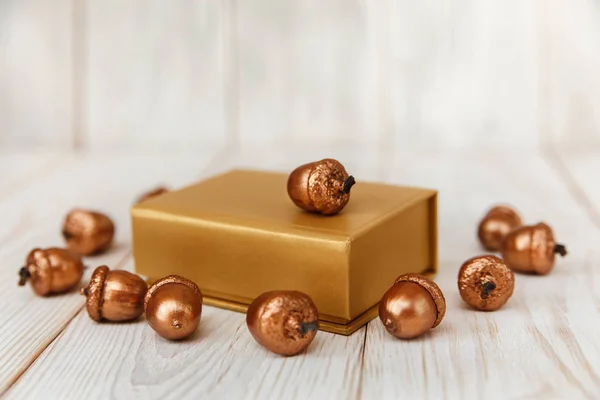 Composizione natalizia.Scatola regalo dorata e ghiande dorate.Tavolo in legno bianco — Foto Stock